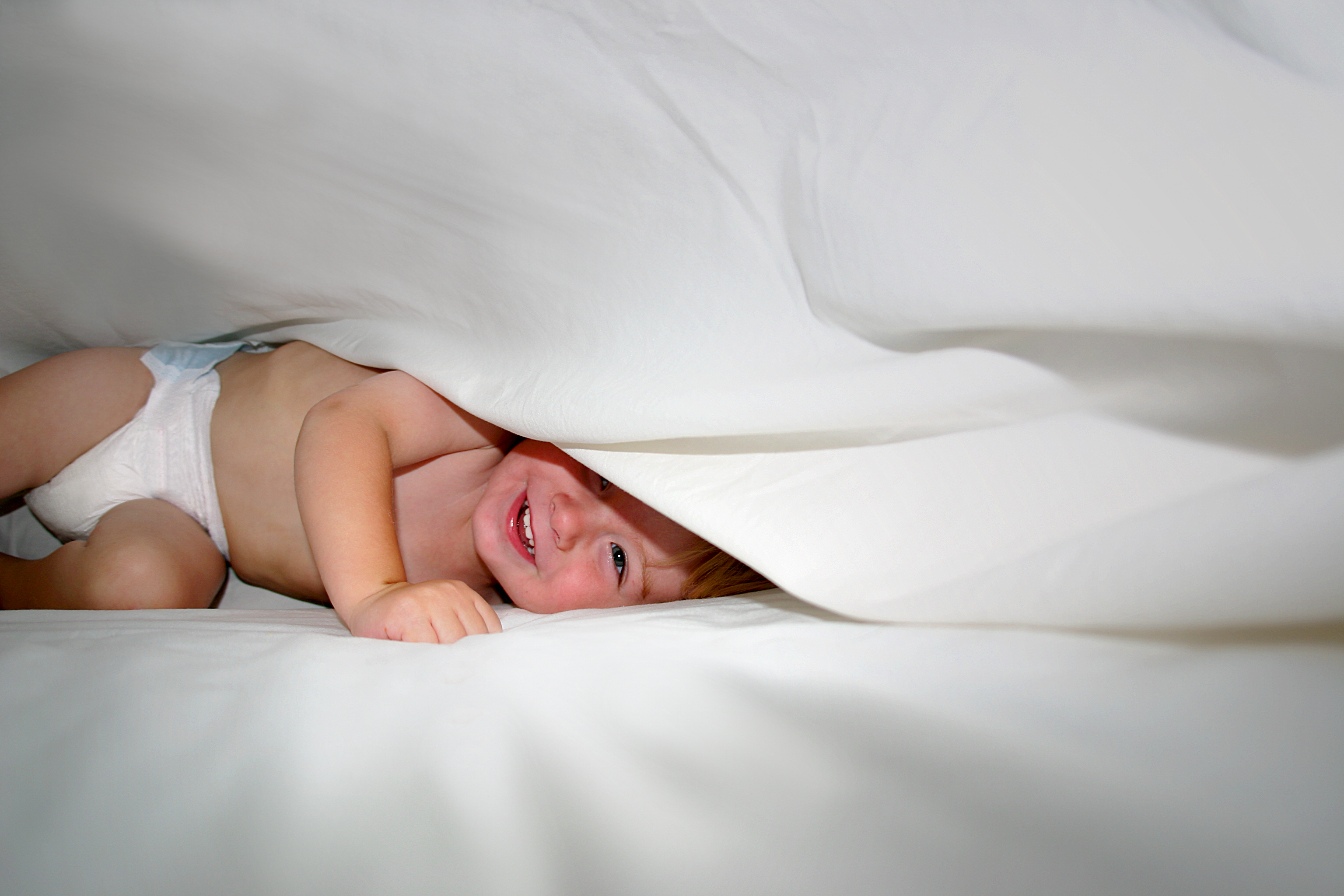 Happy Baby playing under sheets on bed